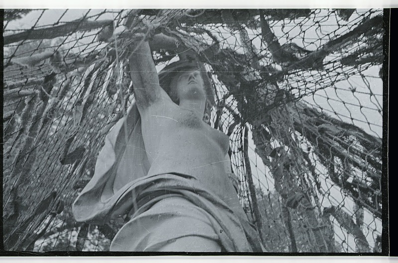 Photographic negative shows a sculpture of a woman covered in camouflage netting, possibly at Versailles.